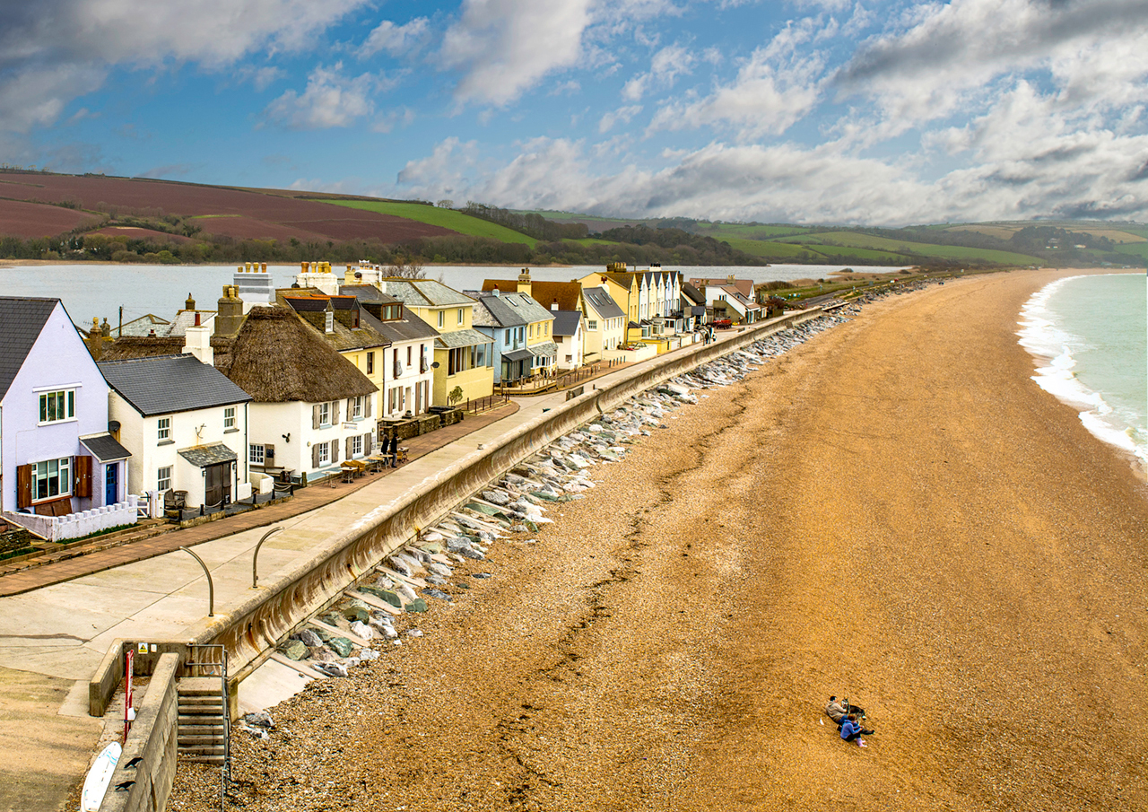 beach cove houses shore pebbles water sea sky landscape village